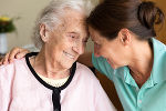 Symbolbild einer älteren Frau und einer Pflegerin, die sich anlächeln.